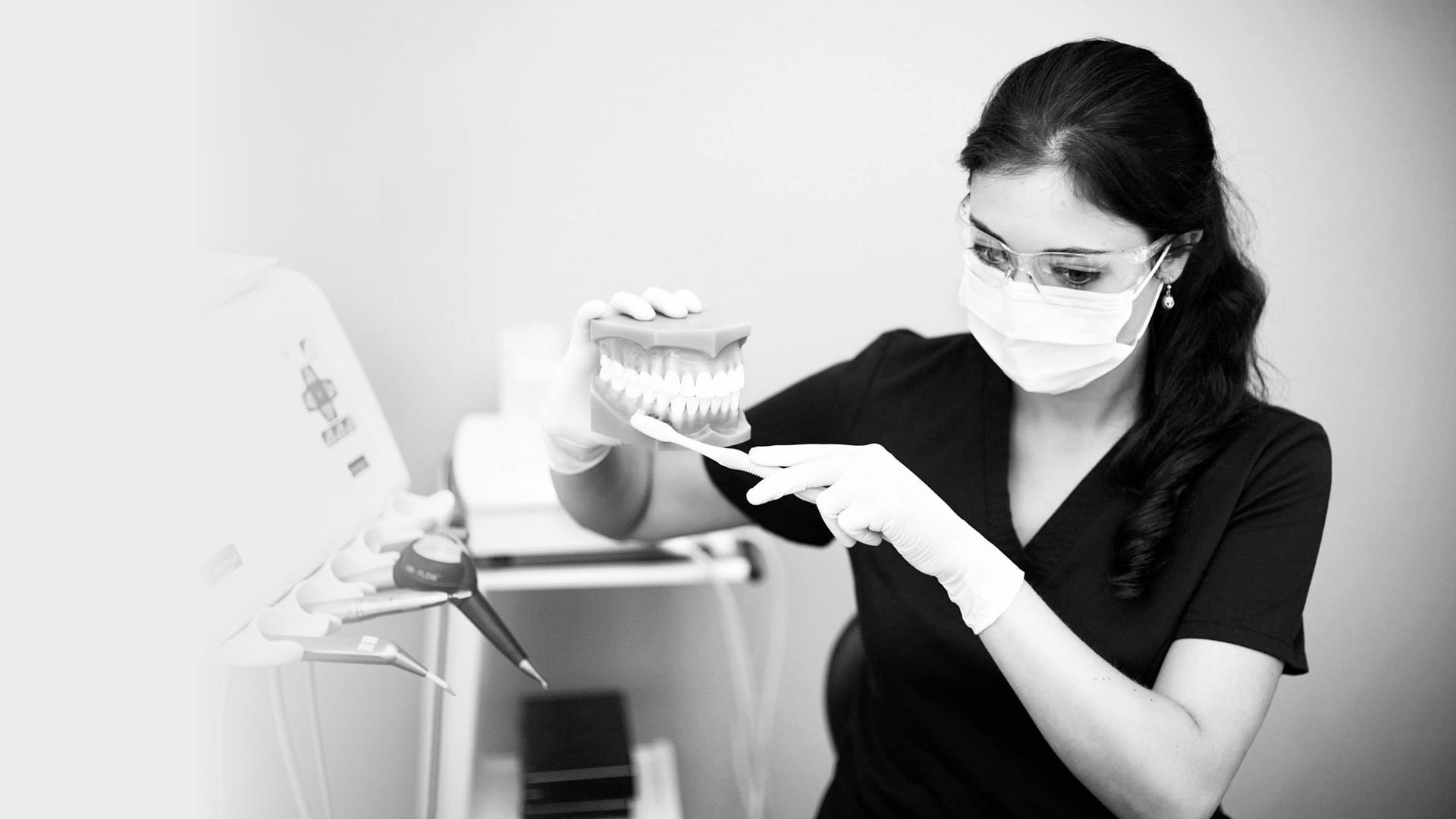 A dentist holds up a model of teeth and shows how to brush them using a toothbrush.