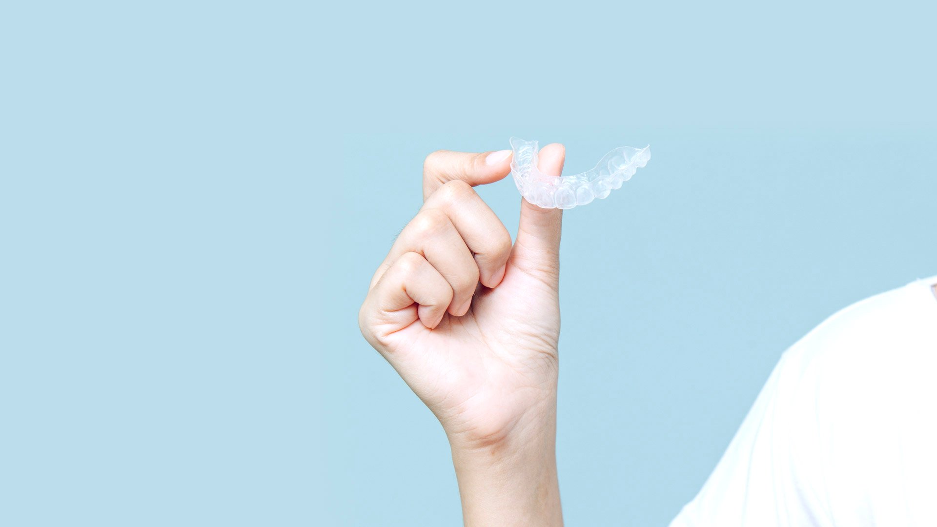 A hand holds an Invisalign clear aligner against a blue background