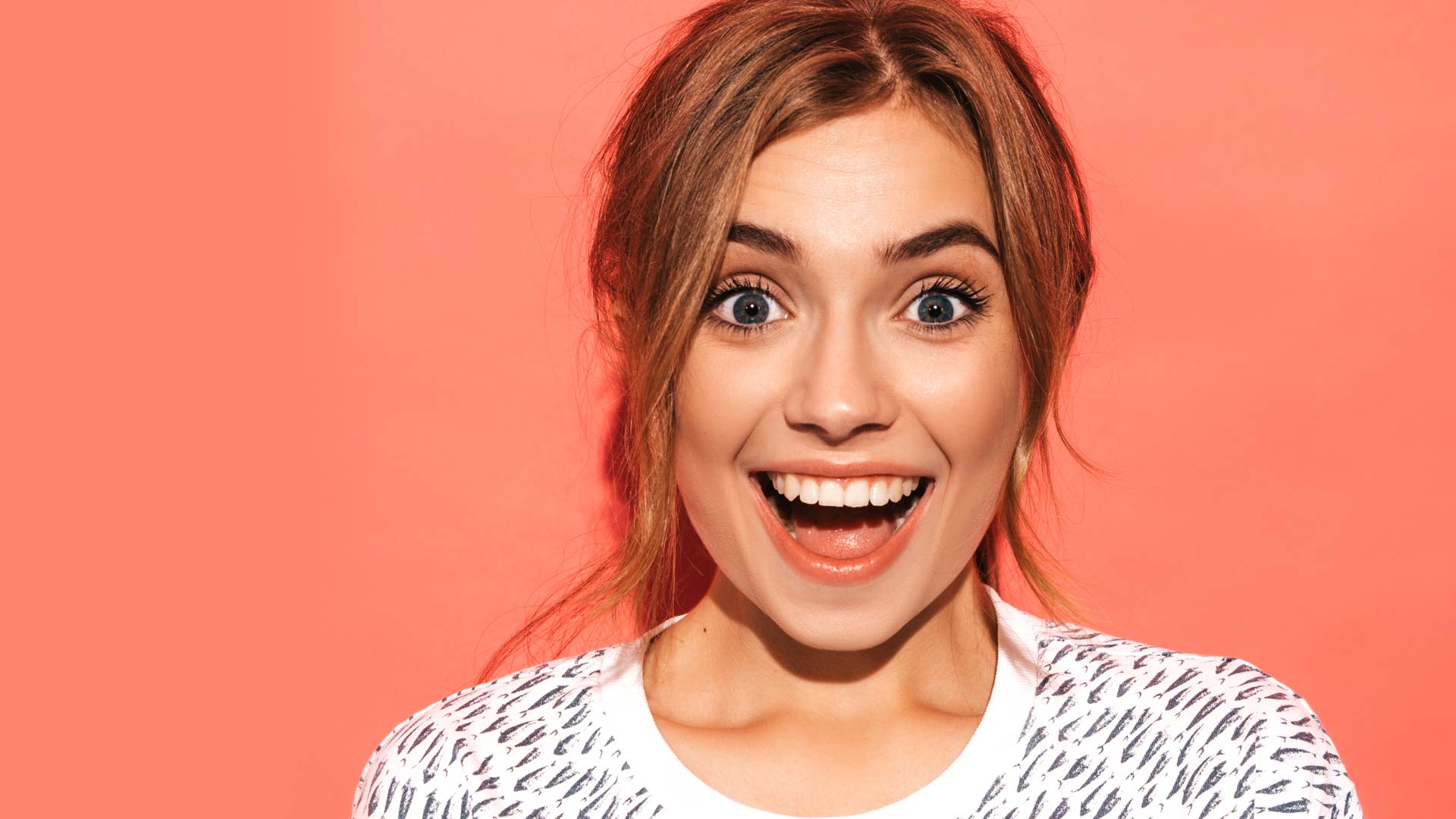 A young woman looks surprised and happy as she smiles at the camera.