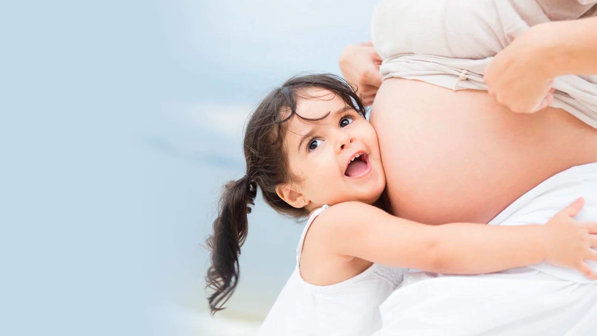 Una niña pequeña escuchando el vientre de su madre embarazada mientras le abraza